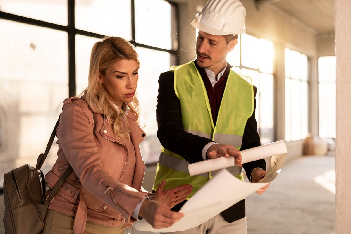Construction worker showing project plans to a client at a building site